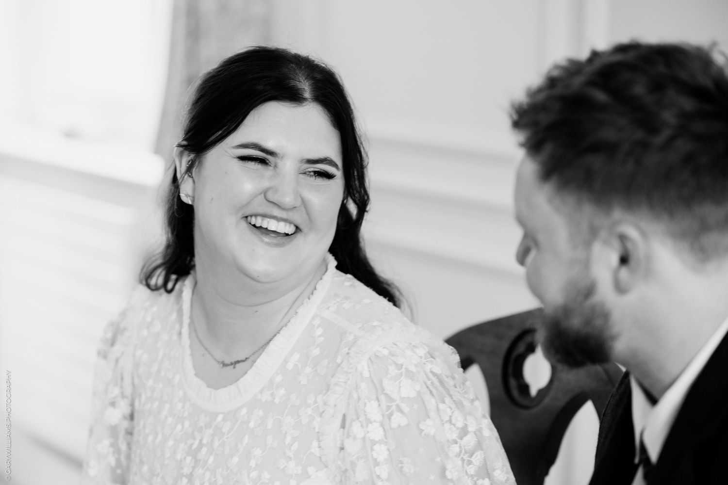 Black and white photo of a smiling bride laughing with groom during wedding ceremony.