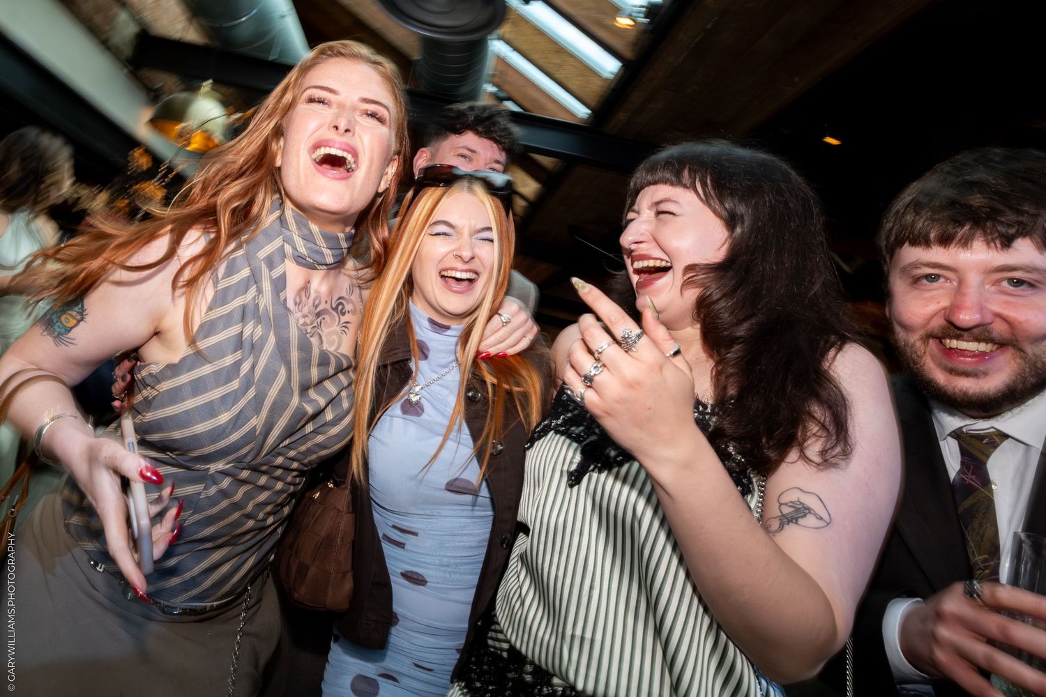 Group of friends laughing and celebrating together at a lively indoor social event or party.