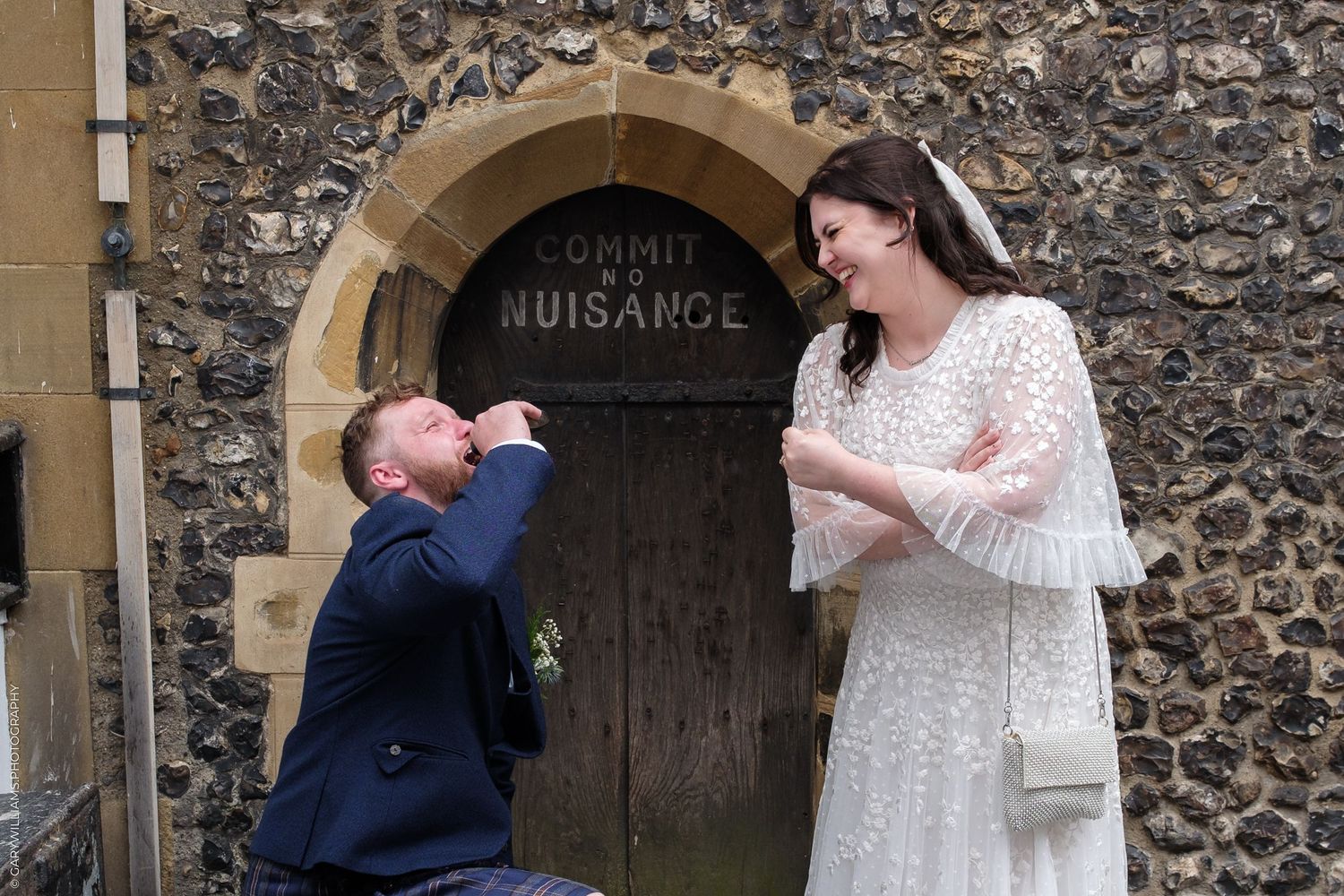 Bride and groom laughing outside church door marked Commit No Nuisance on their wedding day.