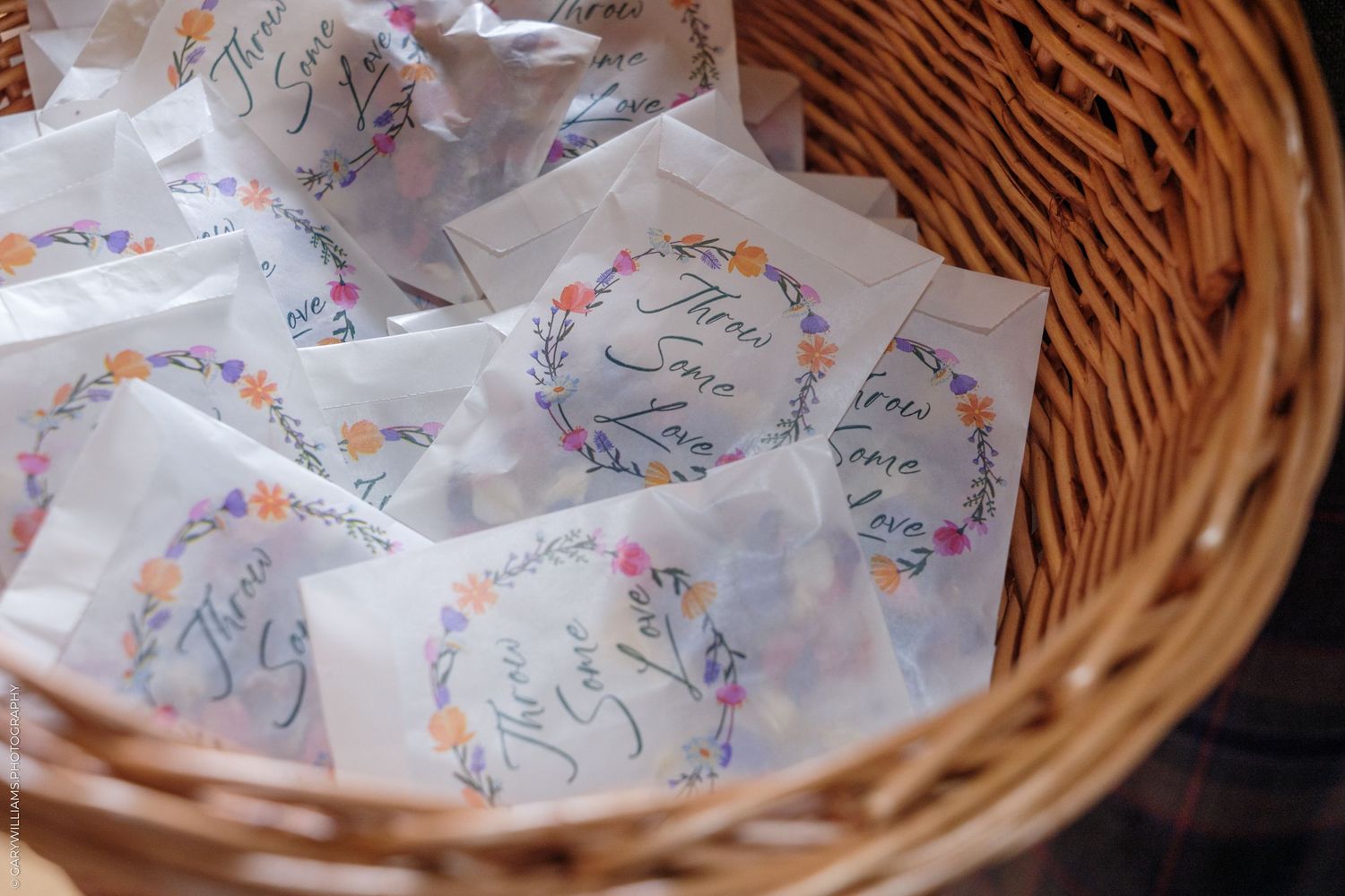 Wicker basket filled with floral-labeled wedding favor seed packets with colorful flower wreath design.