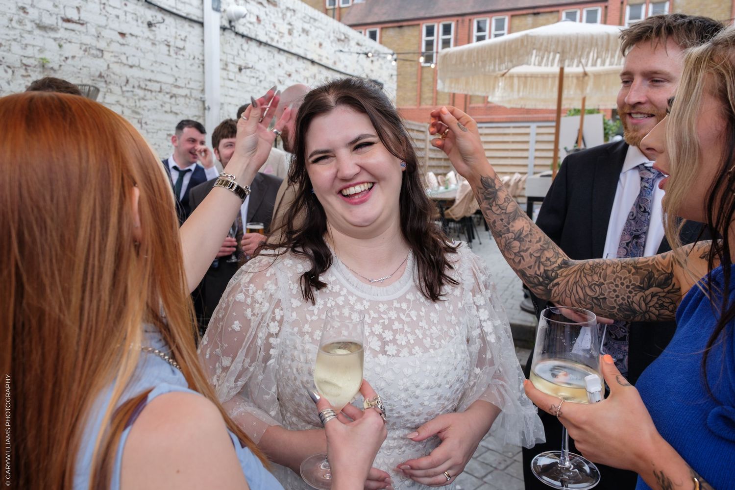 Woman in white lace dress smiling and holding champagne glass at outdoor wedding reception party.