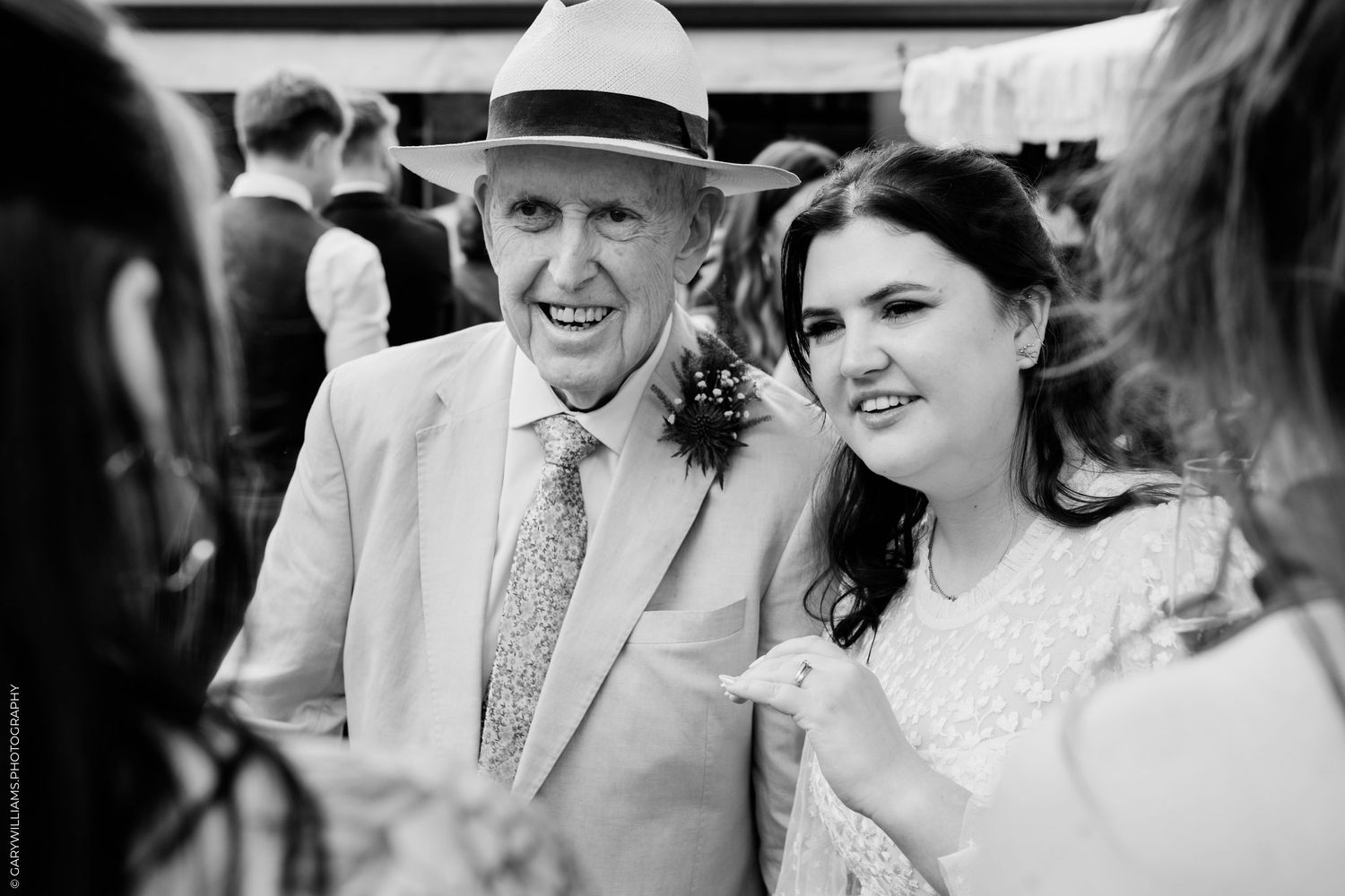 Elderly man in white hat smiles with young woman at wedding reception in black and white photo.