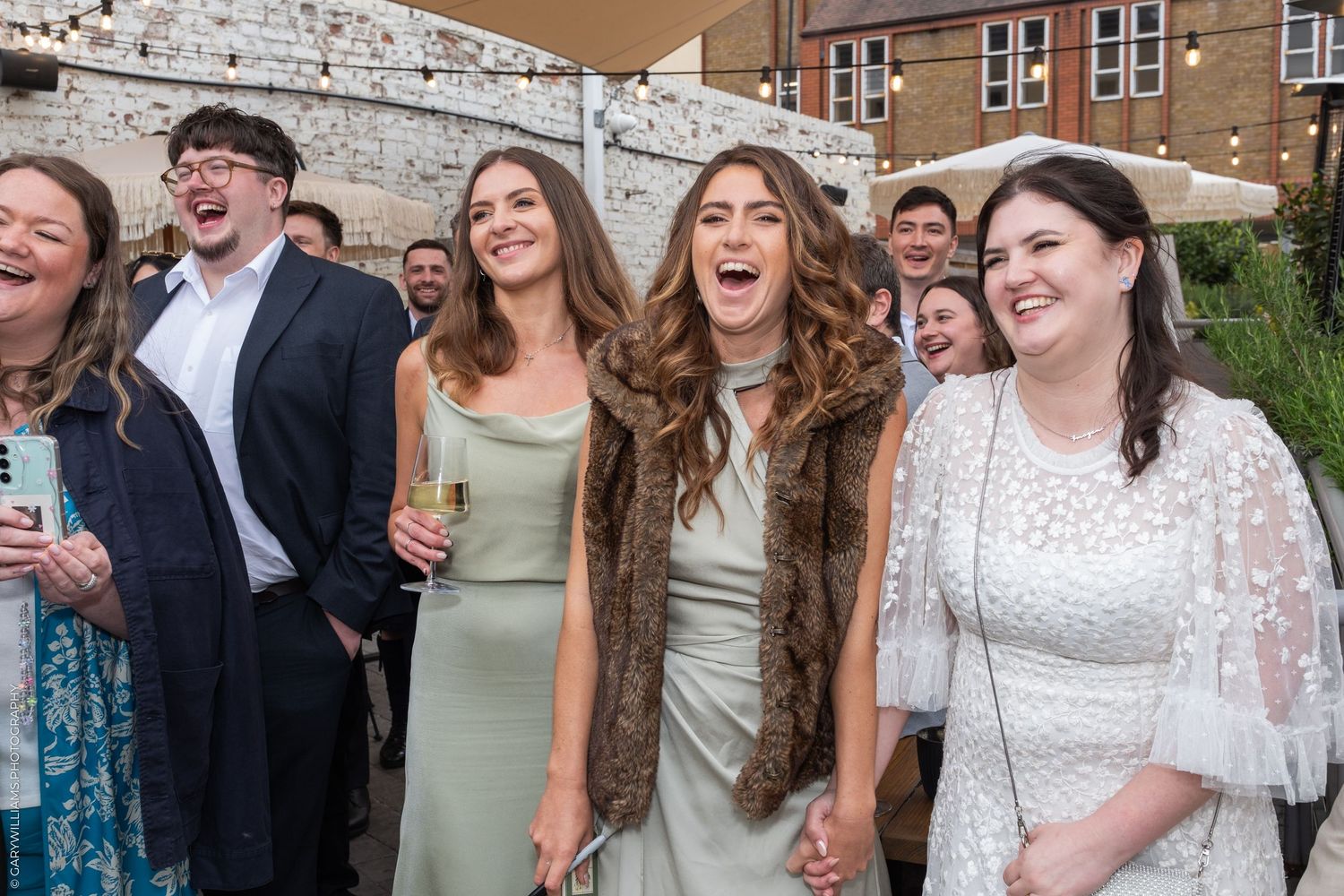 Group of joyful wedding guests laughing and celebrating outdoors at a reception venue.