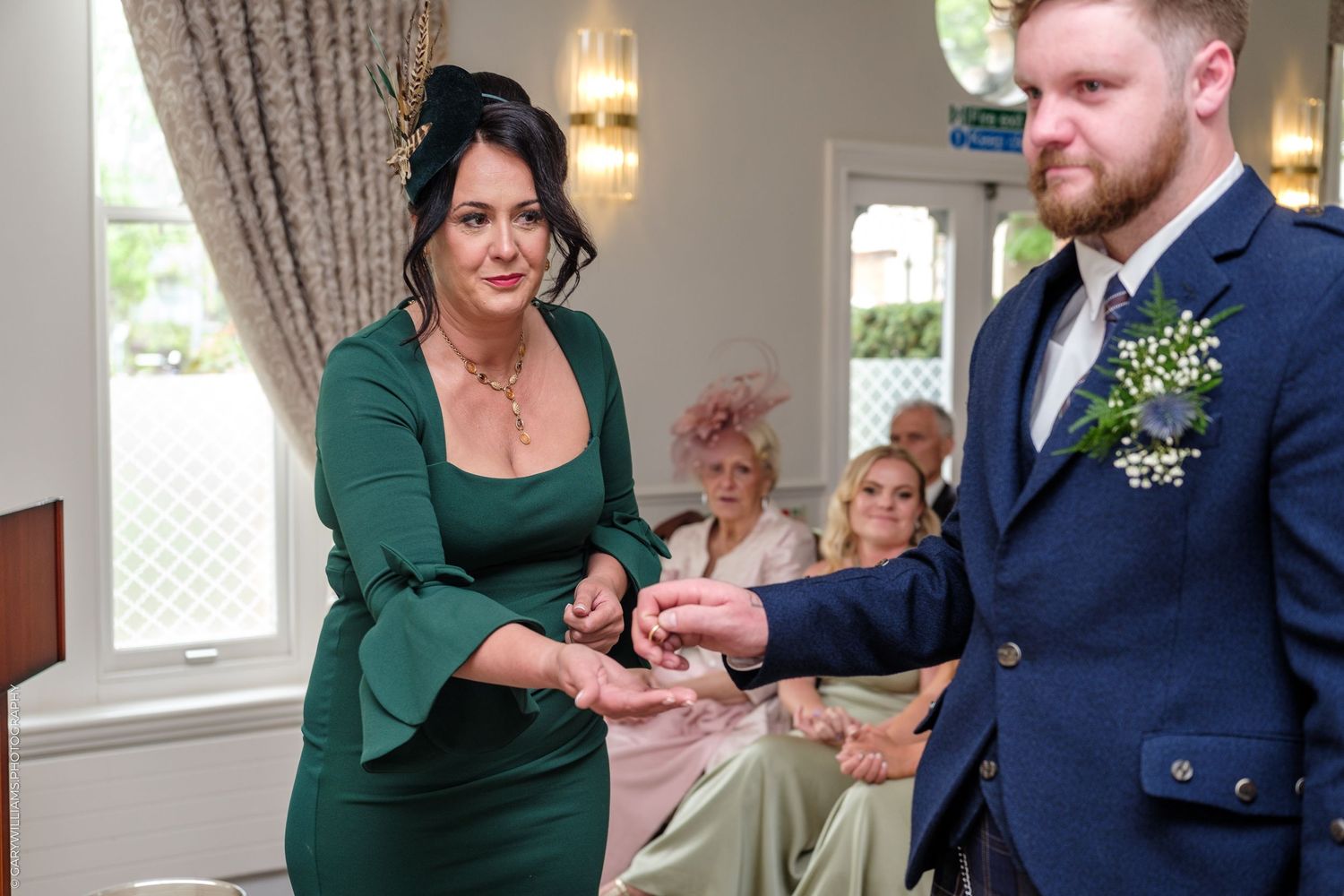 Bride in green dress exchanges rings with groom in navy suit during intimate wedding ceremony.