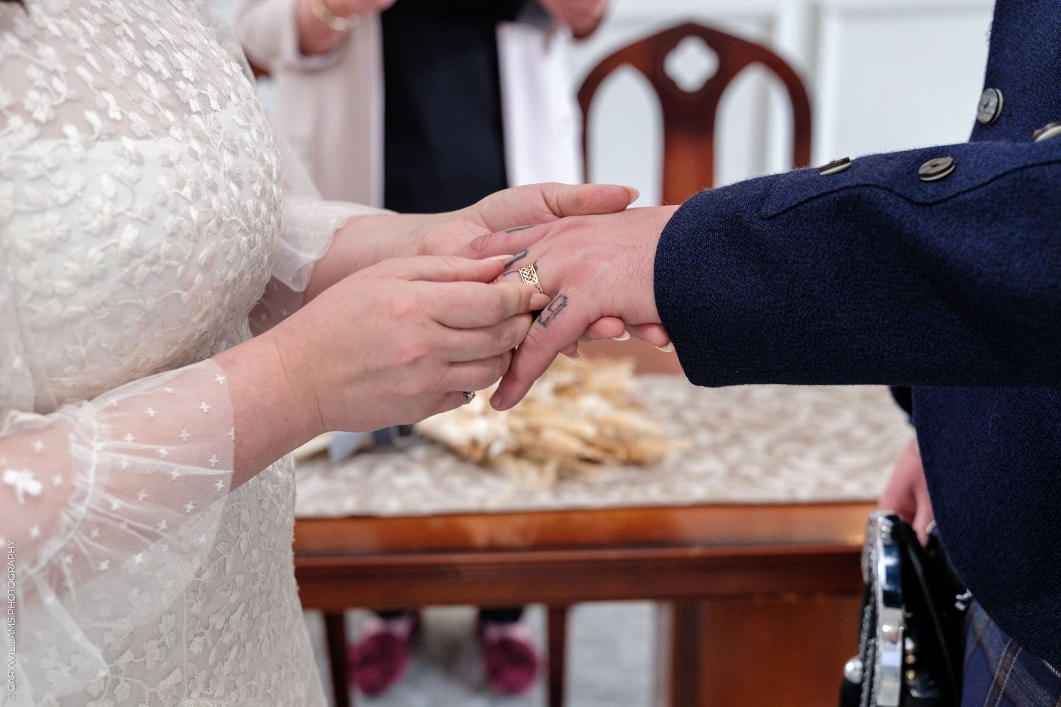 Bride placing a wedding ring on groom's finger during a wedding ceremony, with elegant white lace dress.
