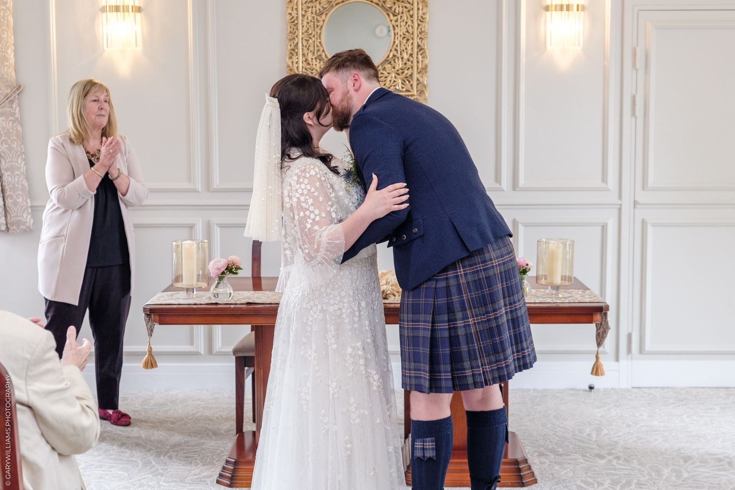 Bride and groom share first kiss in elegant Scottish wedding ceremony, groom wearing traditional tartan kilt.