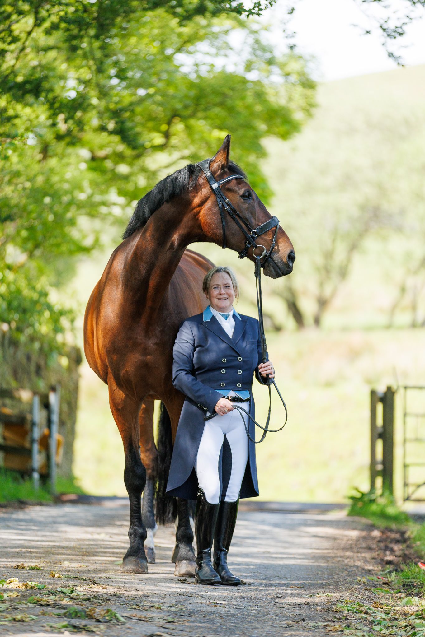 A brown horse and rider in a white sweater pose together against autumn foliage in soft natural lighting.