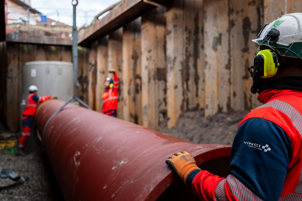 Worker in protective gear inspecting large red pipeline installation.