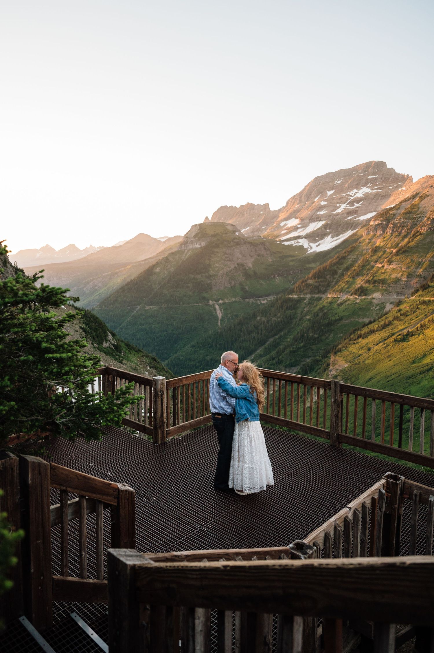 Couple embracing on a wooden overlook deck with stunning mountain valley views at golden hour sunset.