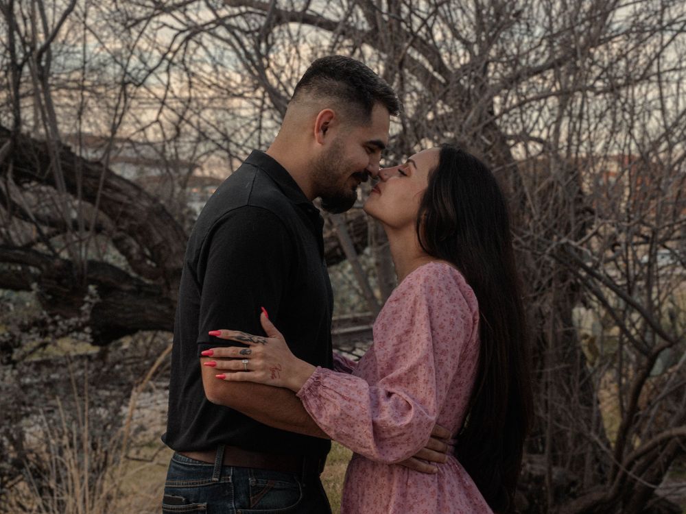 Couple sharing a romantic almost-kiss embrace surrounded by bare winter trees outdoors.