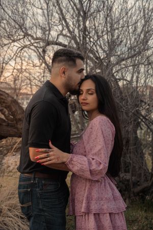 Couple sharing an intimate embrace at sunset with bare trees in the background.
