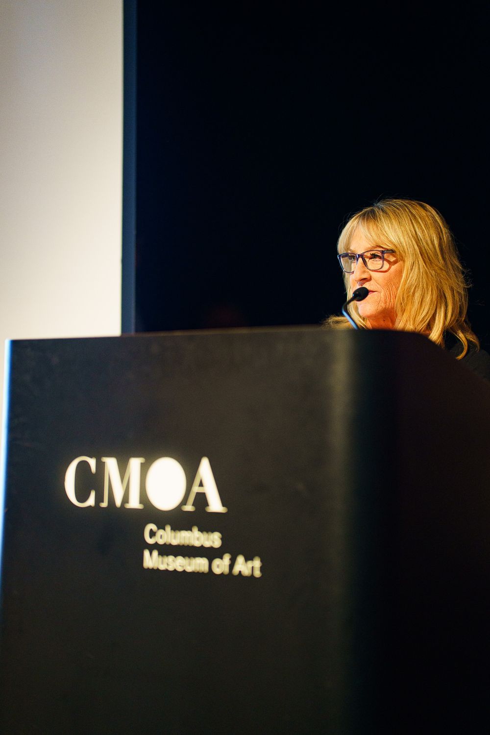Woman speaking at CMOA Columbus Museum of Art podium during a formal presentation event.