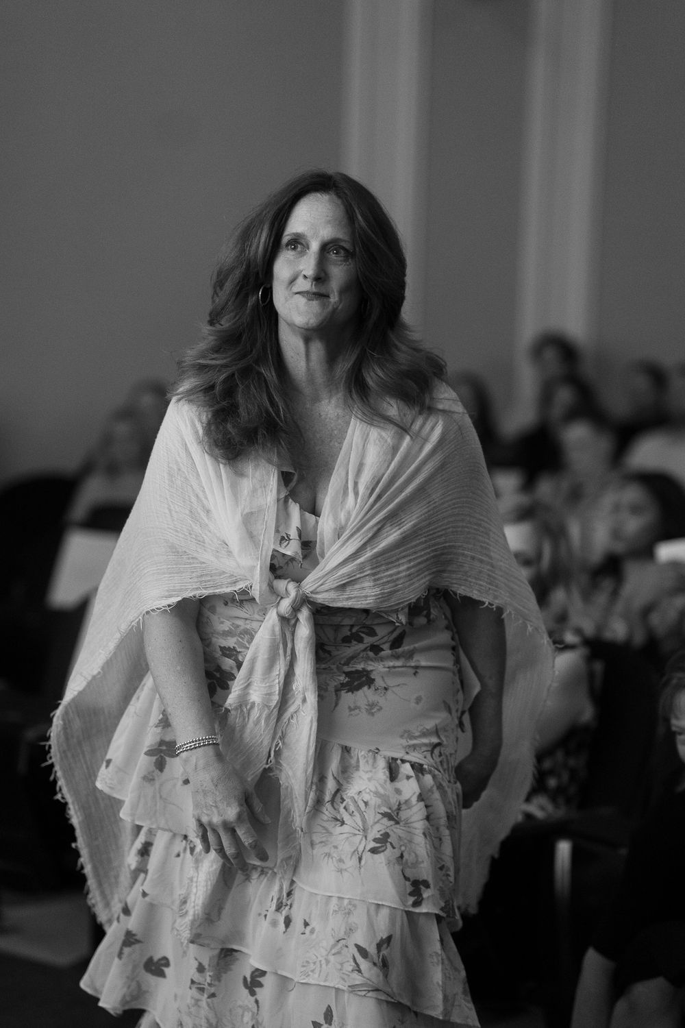 Black and white photo of a woman in a floral dress and shawl walking gracefully at an event.