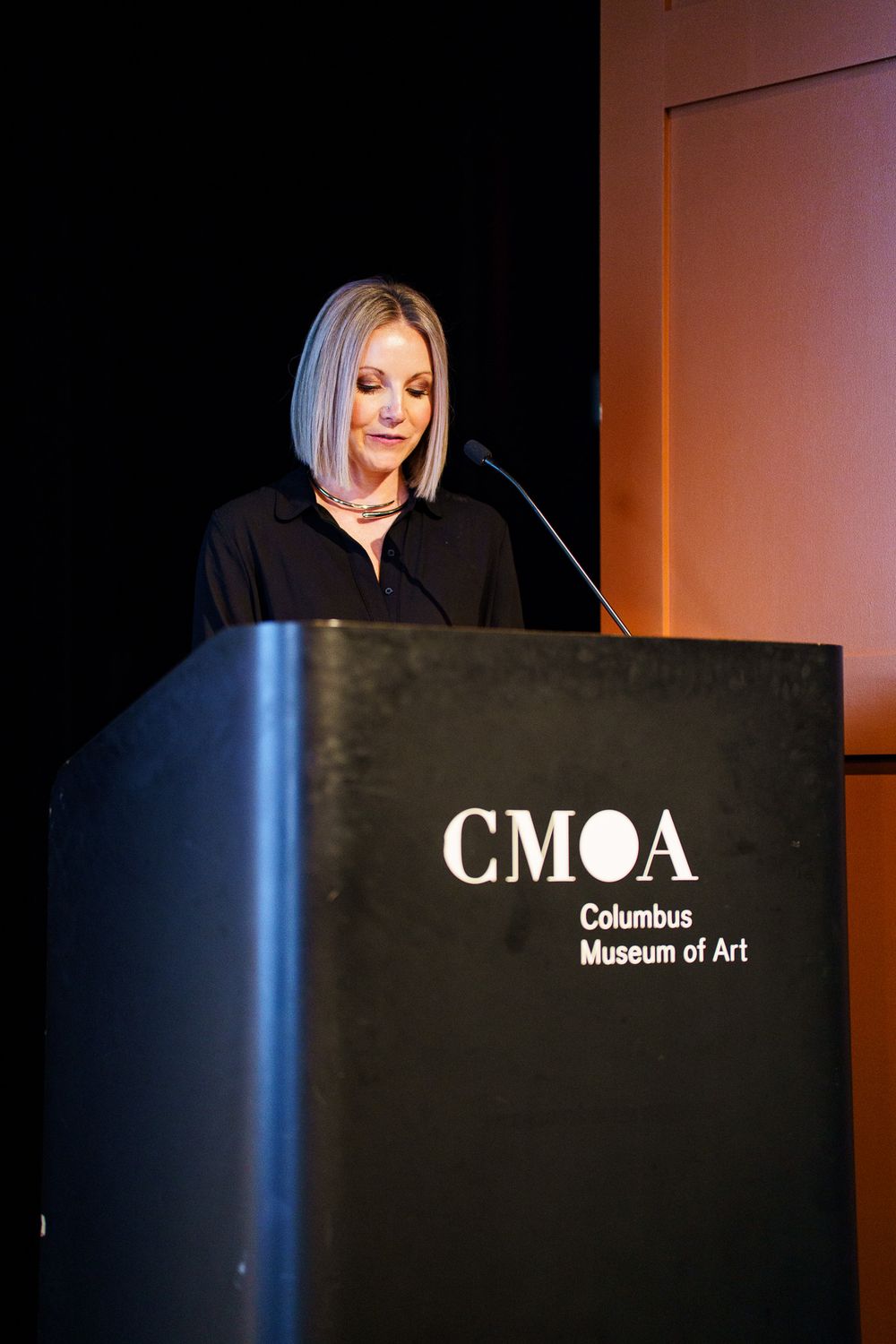 Woman with blonde hair speaks at CMOA Columbus Museum of Art podium during formal event.