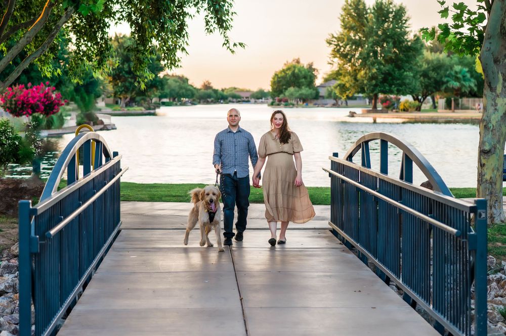 Couple walking golden retriever on blue bridge by a scenic river at golden hour.