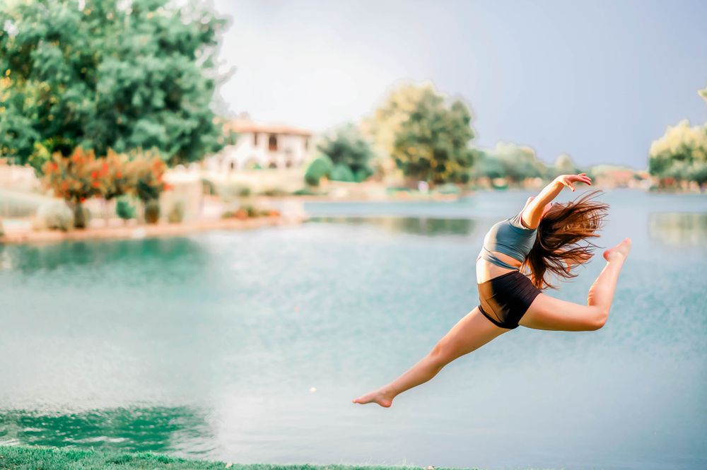 Athletic woman performing a graceful leap over a serene lake surrounded by lush green trees.