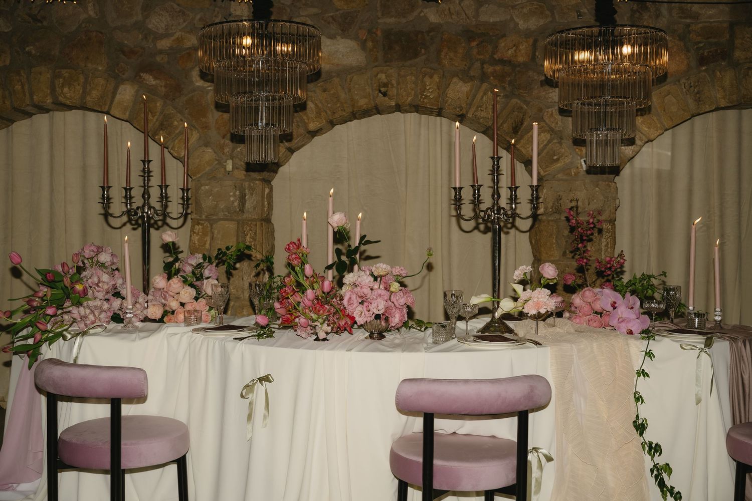 Elegant stone wall venue decorated with pink flowers and white curtains.