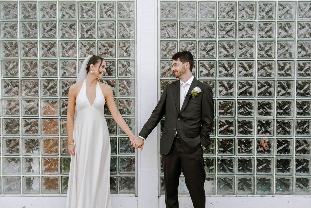 A romantic wedding couple poses against a glass block wall in an artistic sequence of photos.