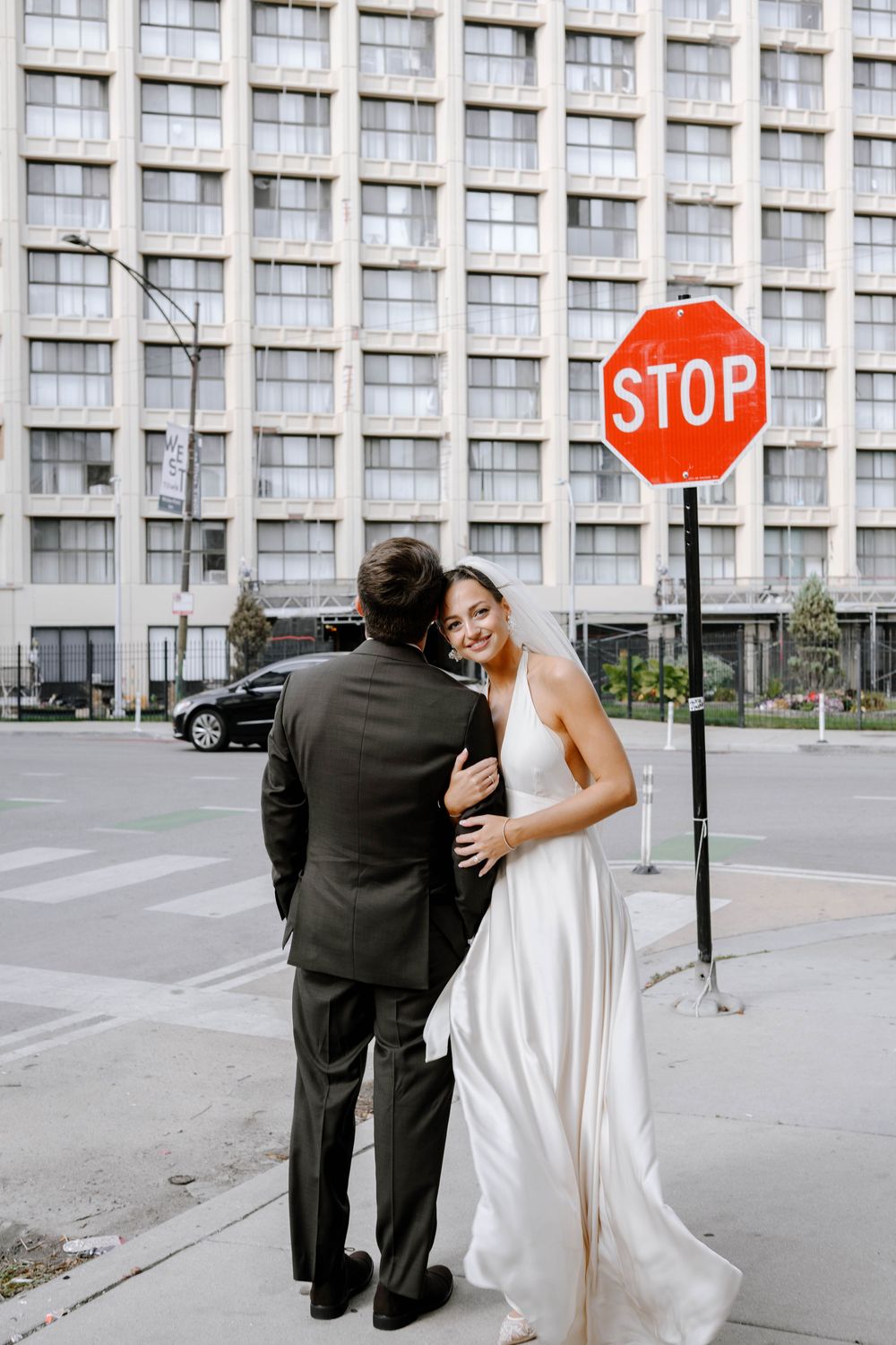 A wedding couple poses playfully by a stop sign in front of an urban building.