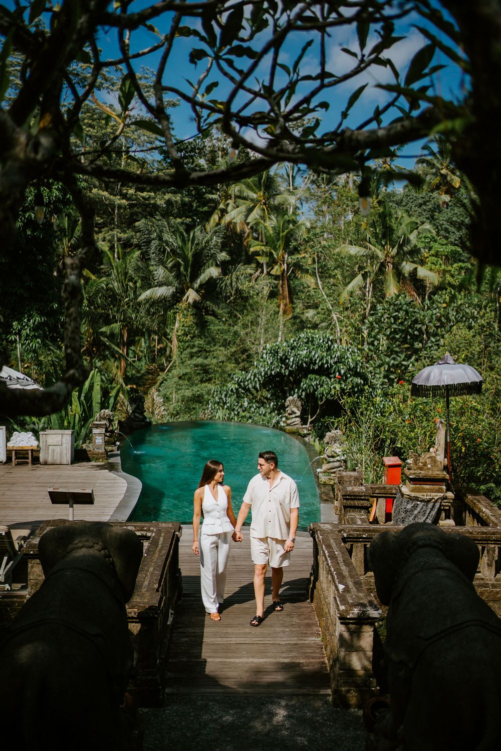 Couple explores stone pathways and tropical gardens near resort infinity pool.