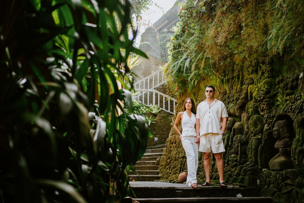 Couple walking through lush green corridor with hanging vines and tropical plants.