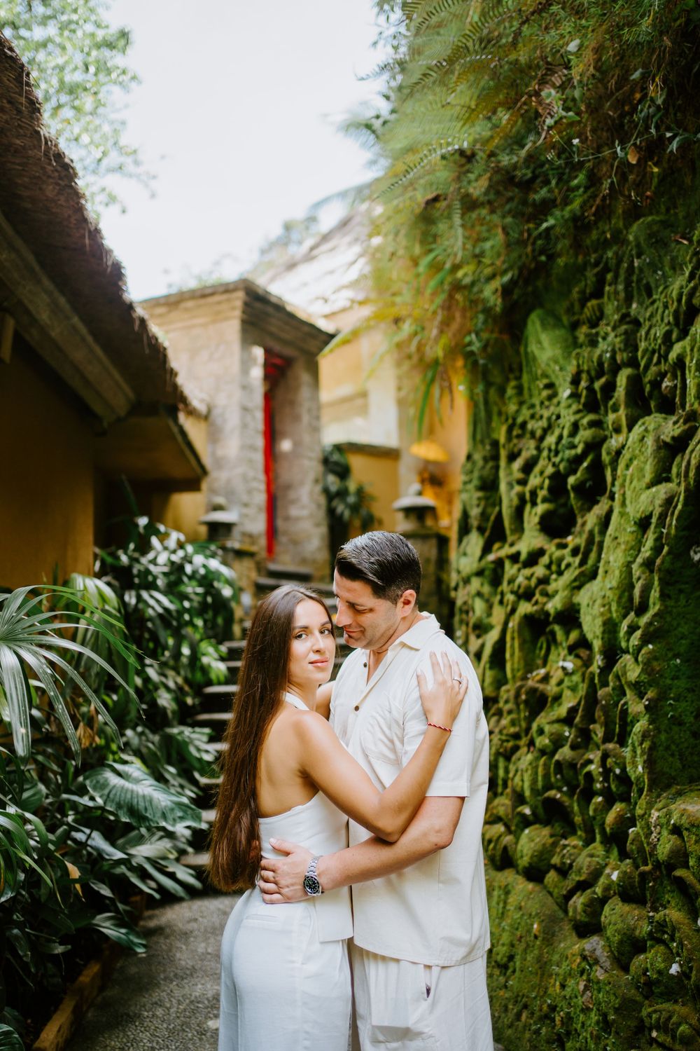Tender embrace captured in a garden pathway with stone walls and tropical plants.