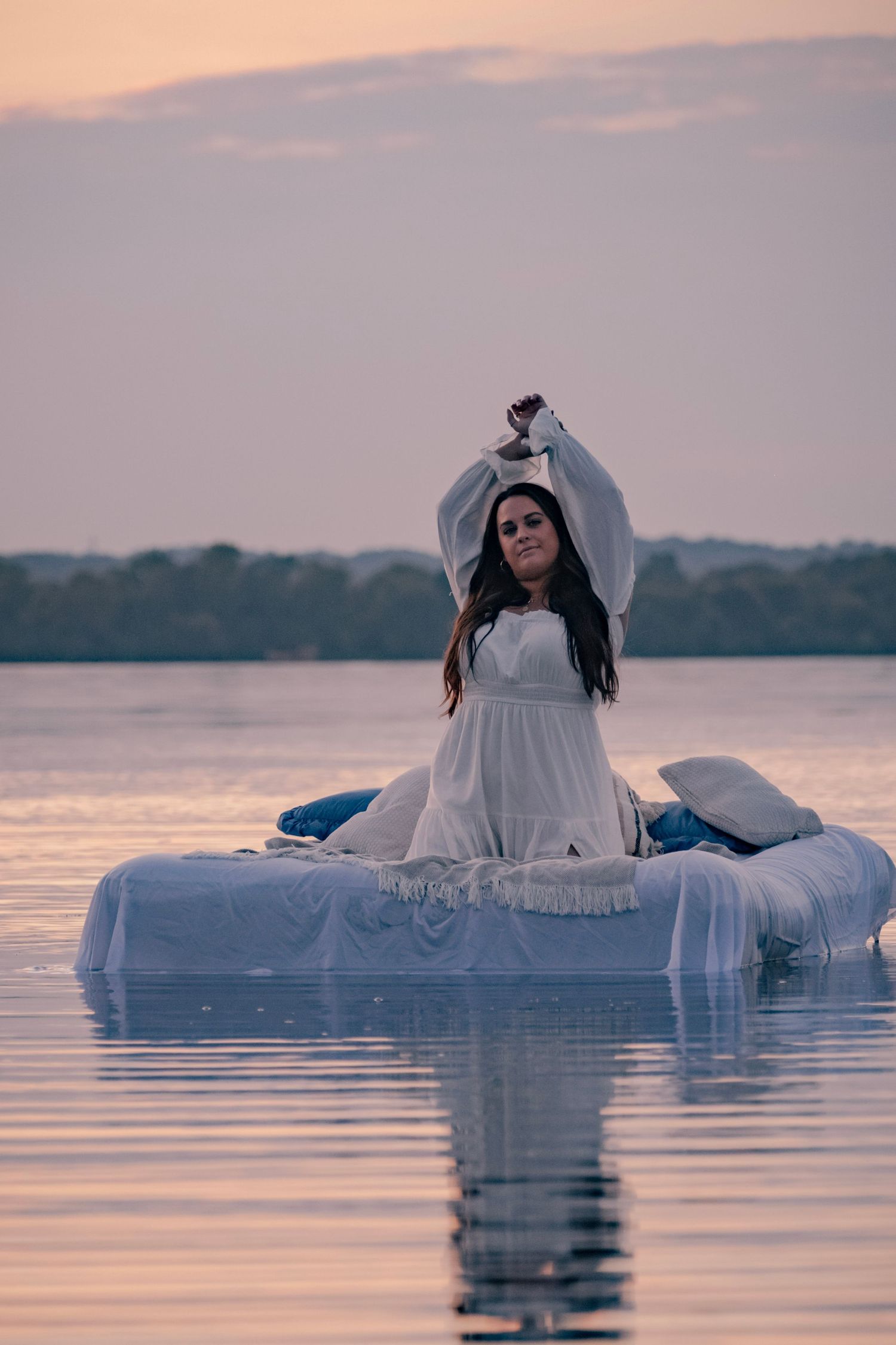 A figure in a white dress floats serenely on calm waters during sunset creating a dreamy ethereal scene.