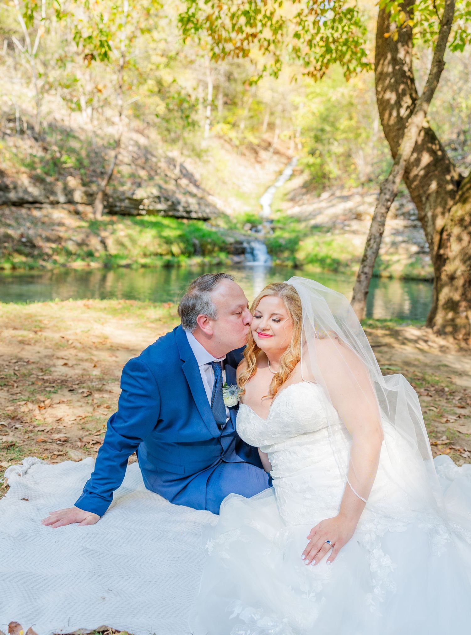 A romantic wedding couple shares a dip kiss on a hilltop overlooking a scenic lake at sunset at Dogwood Canyon by Janie Loftin Photography.