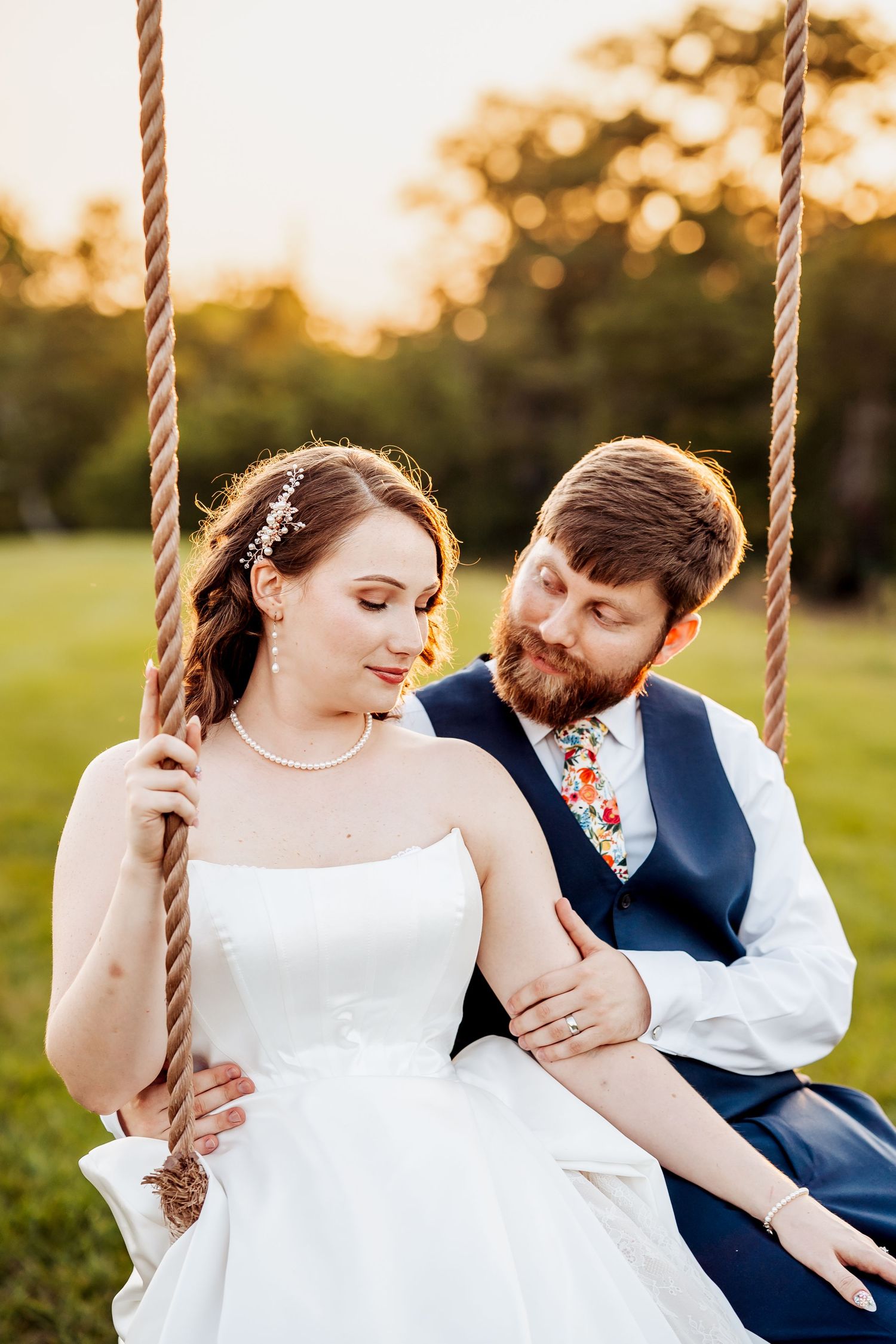 A romantic wedding couple shares sweet moments on rope swings at sunset in a dreamy outdoor setting.
