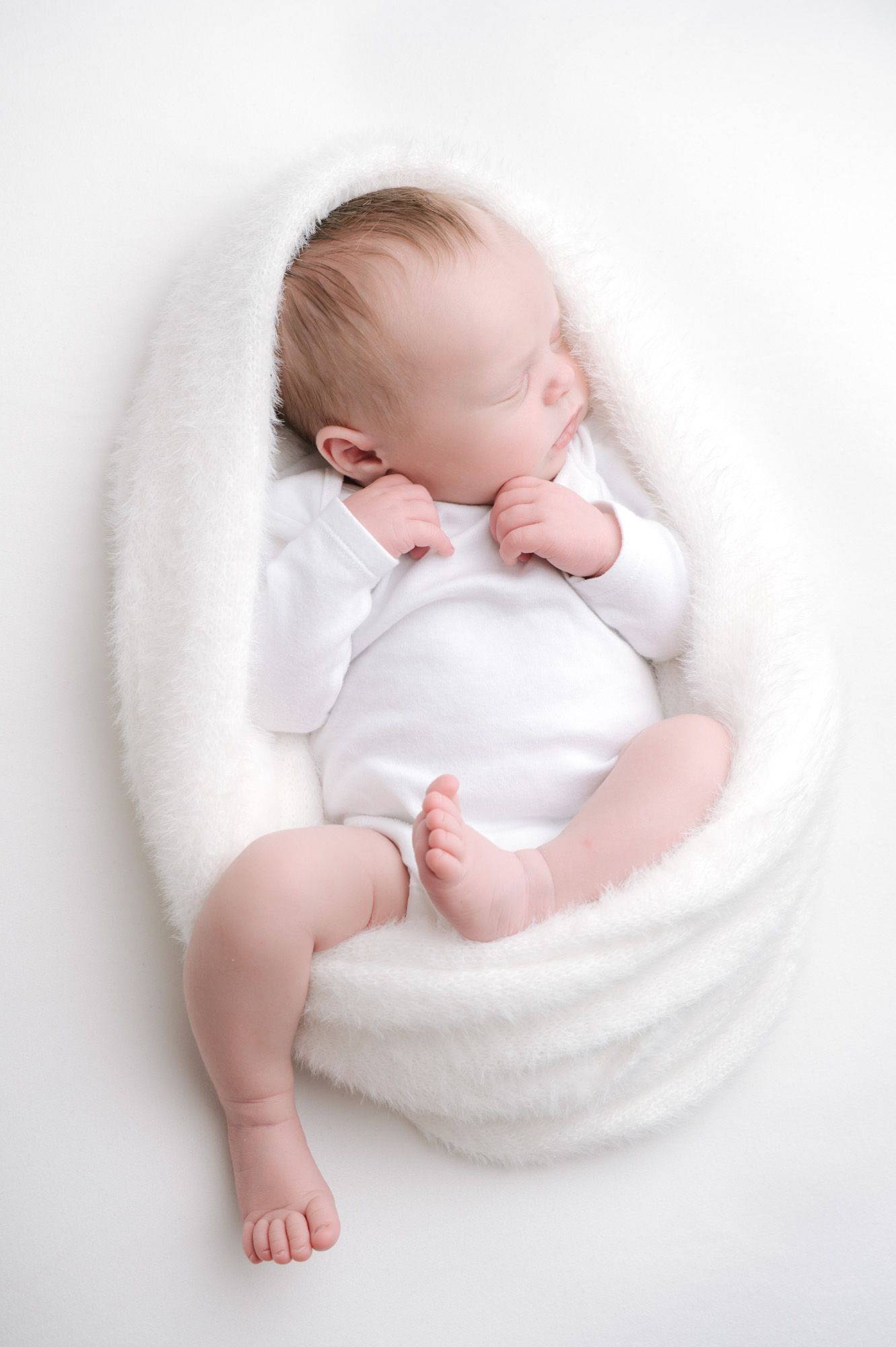 Newborn baby sleeping peacefully on white blanket.