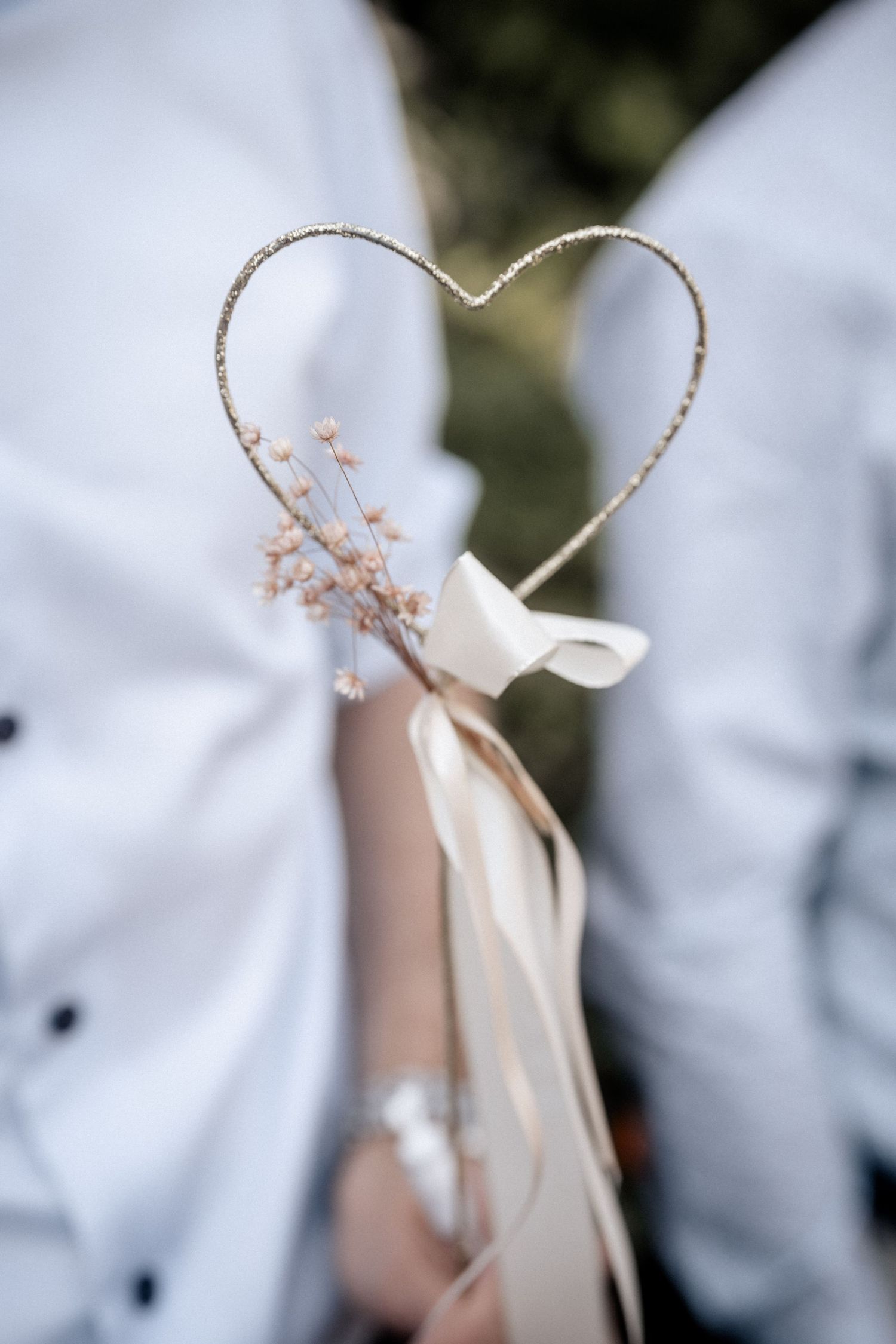 A delicate wire heart decoration with cream ribbons and dried flowers creates a romantic wedding accessory detail.