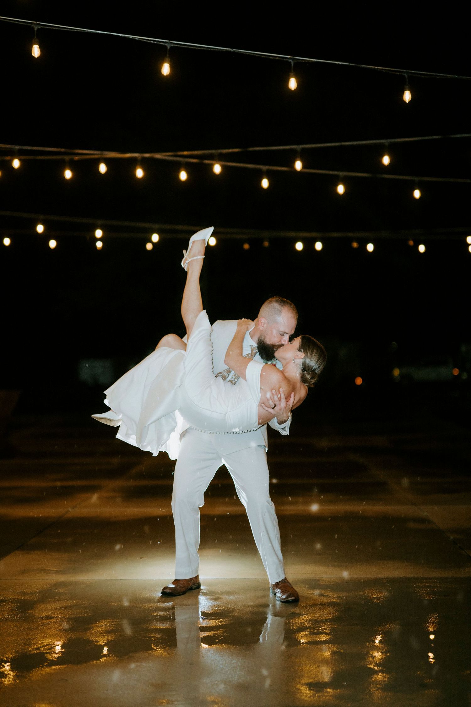 A figure in white performs an artistic dance move under twinkling string lights at night.