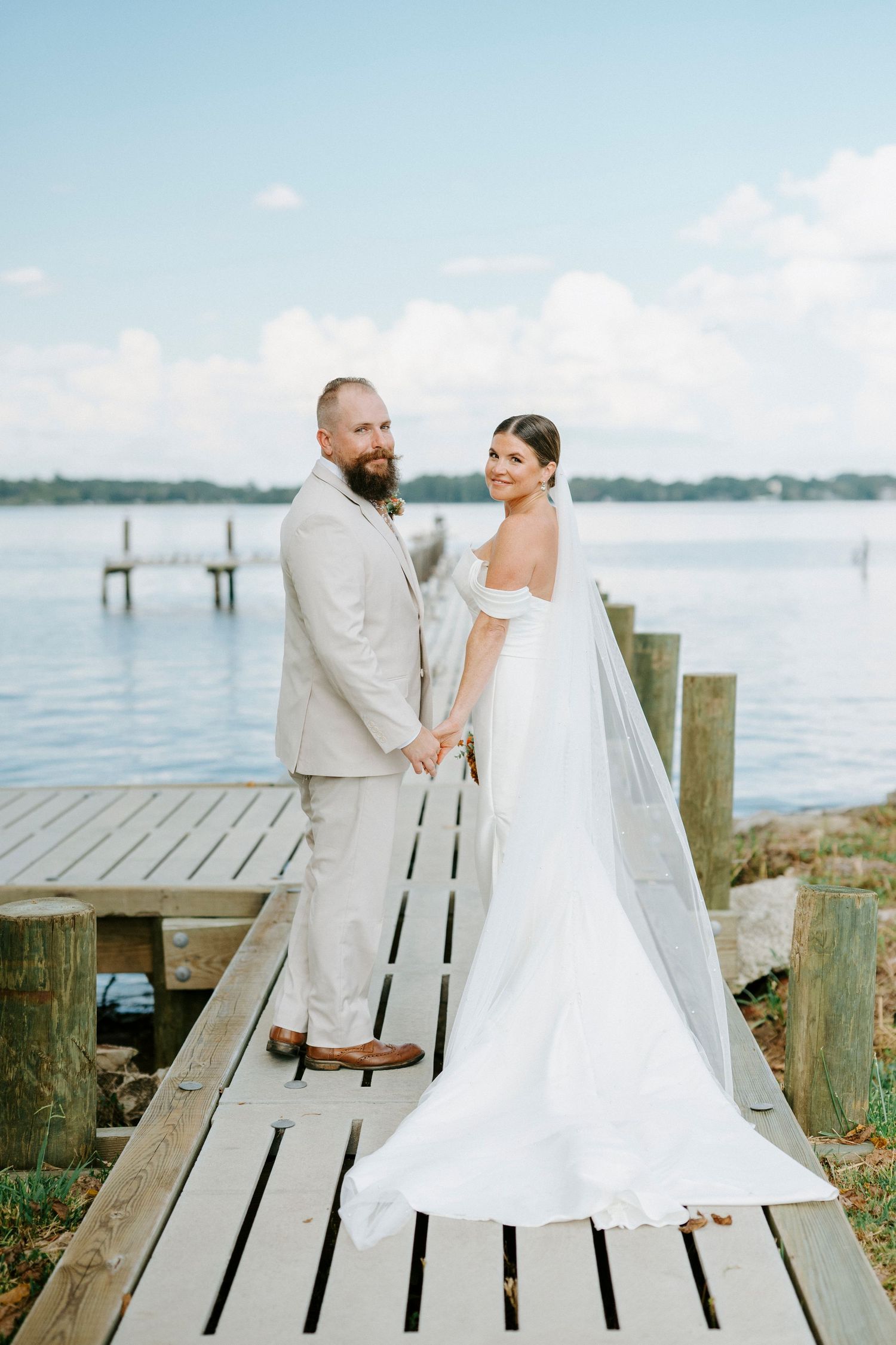 A romantic wedding couple poses together on a wooden dock overlooking a serene waterfront on their special day.
