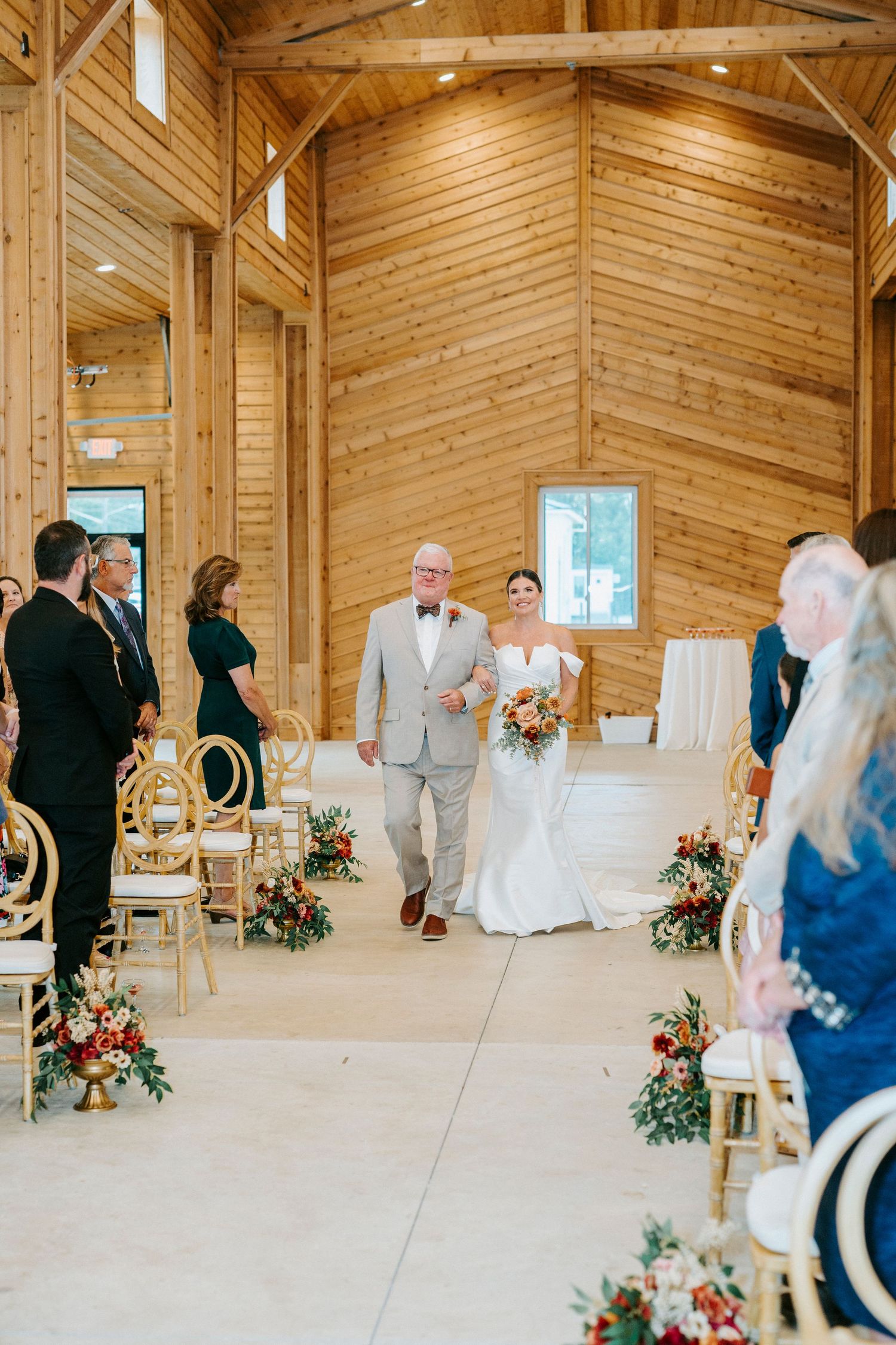 A wedding ceremony in a rustic wooden barn venue with elegant white chairs and floral aisle decorations.