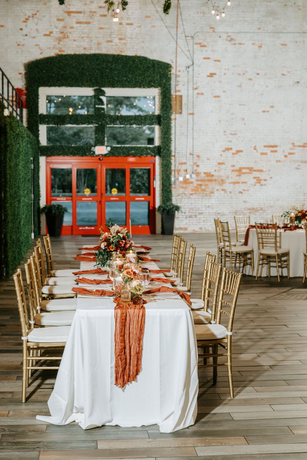 An elegant wedding reception table with white linens, gold chairs, and terracotta accents in an industrial-style venue.