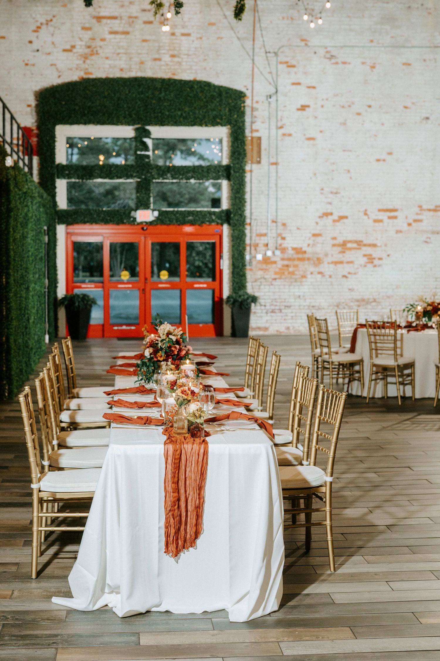 An elegant wedding reception table with white linens, gold chairs, and terracotta accents in an industrial-style venue.