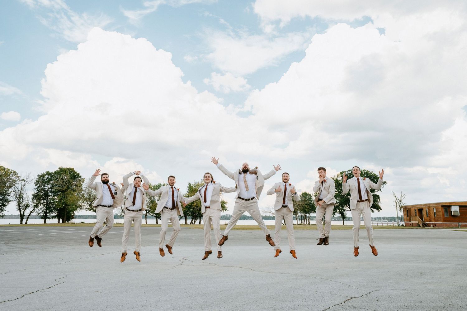 Wedding party members in white outfits jumping in synchronized motion against a cloudy sky background.