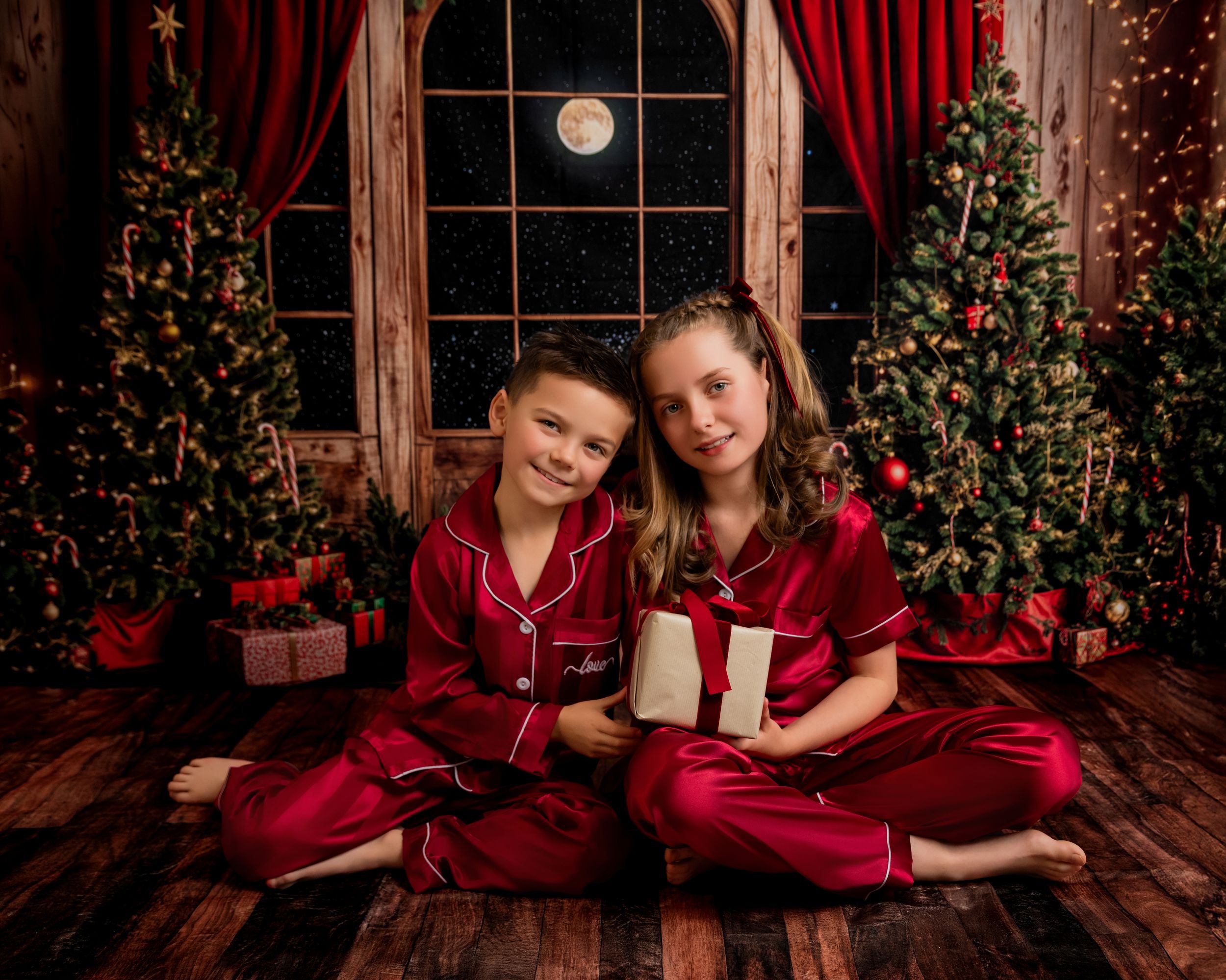 Holiday portrait session with two people in matching burgundy outfits against a festive Christmas backdrop with window.