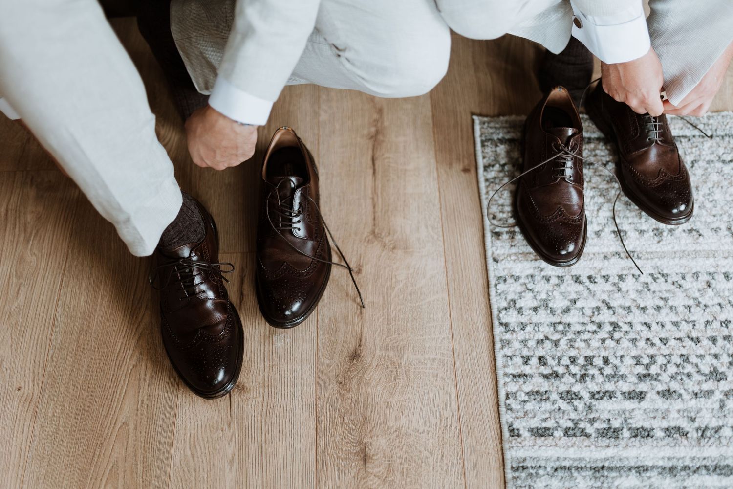 Five beige linen suit jackets hanging in a row on a white wall with dark floral wallpaper visible in the background.