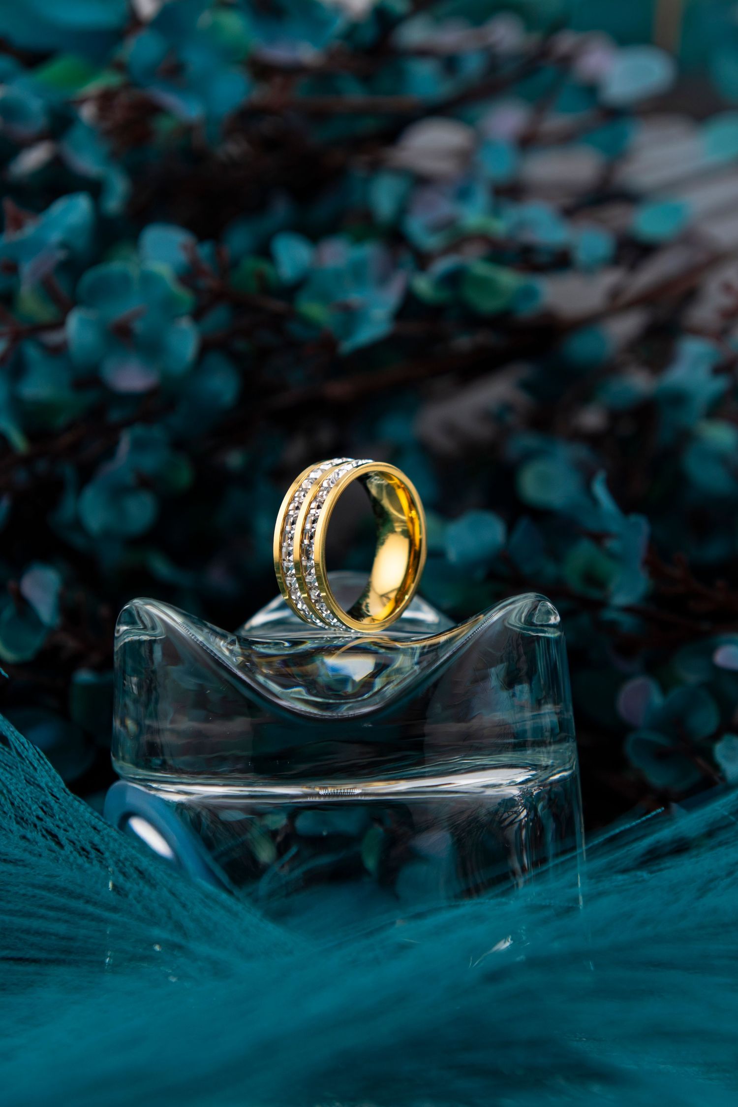 Gold wedding rings artistically displayed on glass surface with teal background.