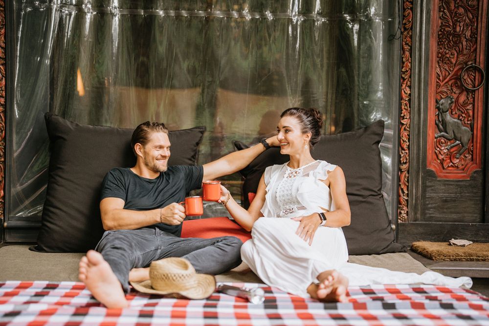 Couple relaxing on picnic blanket against rustic wall with vintage decor.
