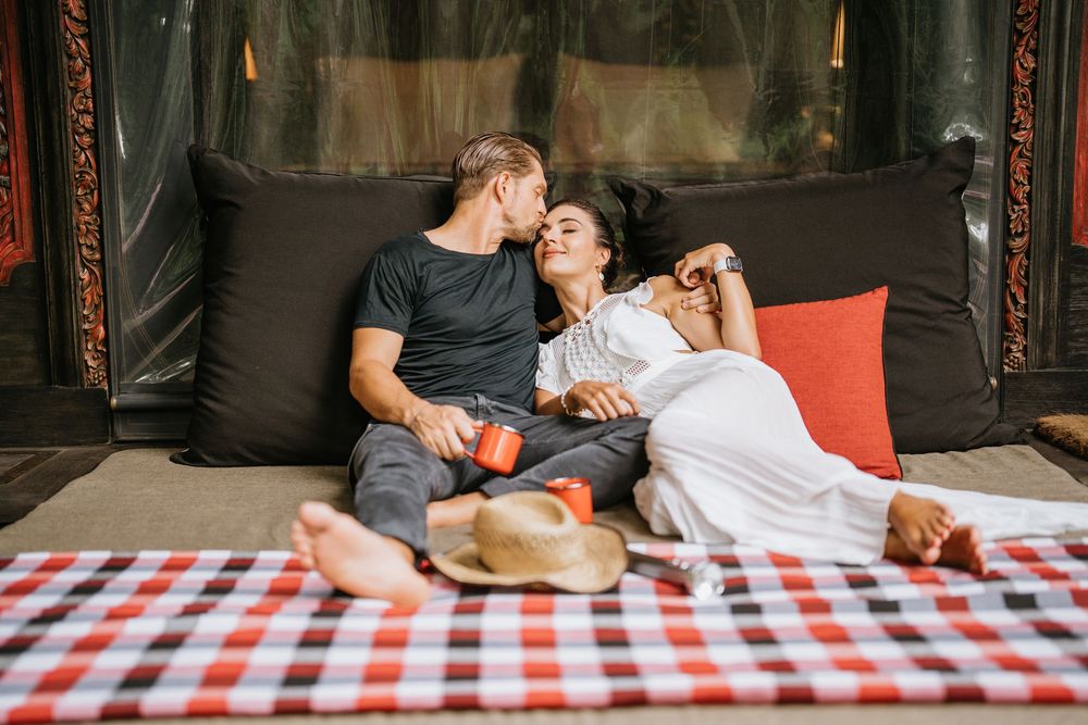 Couple lounging together on red and white checkered surface with playful expressions.