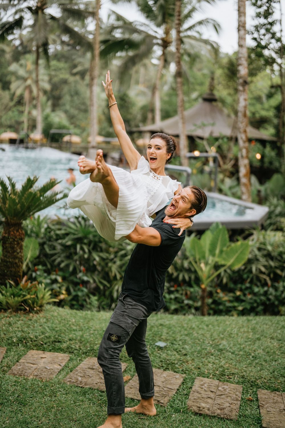 Couple dancing and twirling in a lush tropical garden with palm trees in the background.