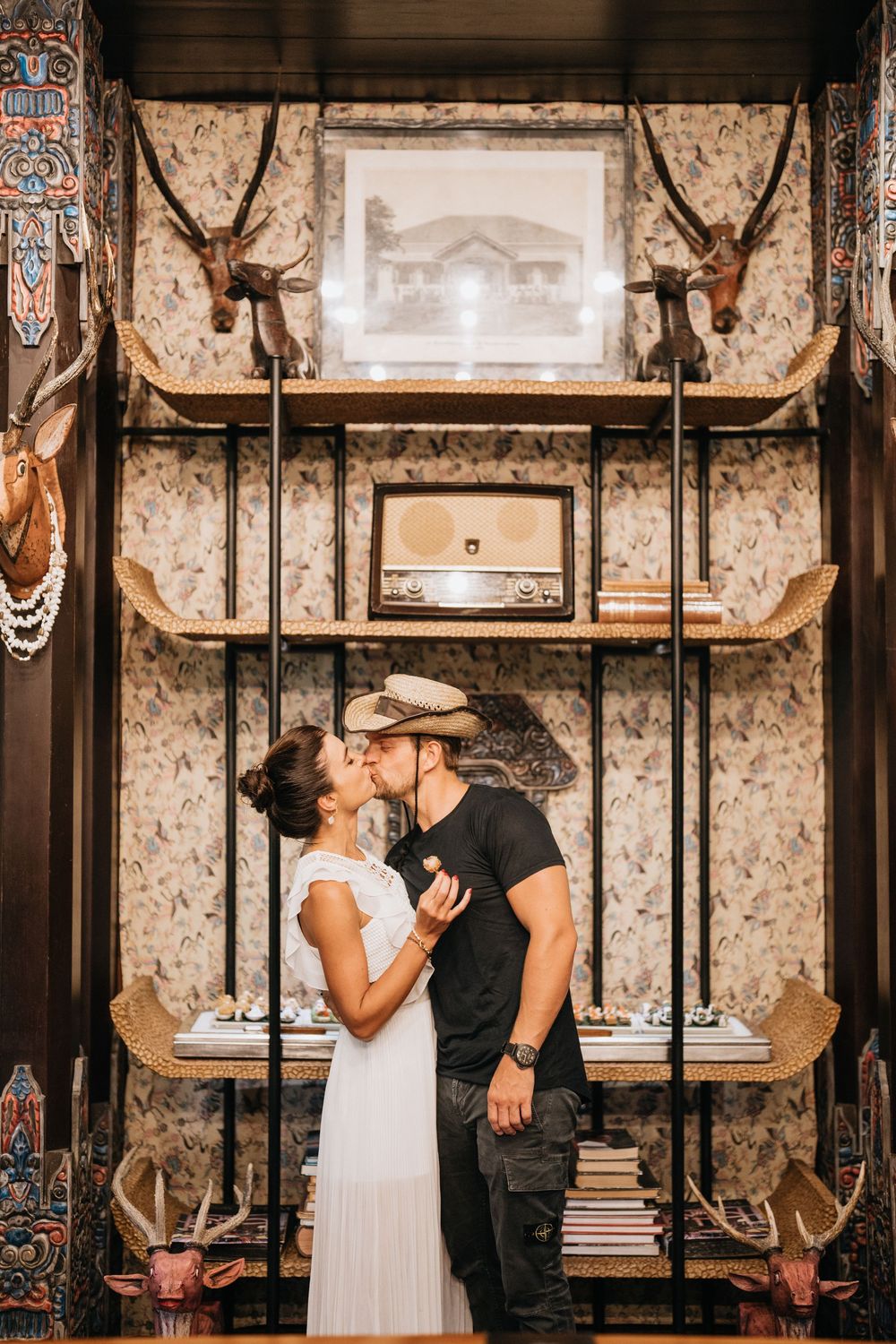 Couple sharing intimate moment in vintage room with antique wall decorations and mounted antlers.