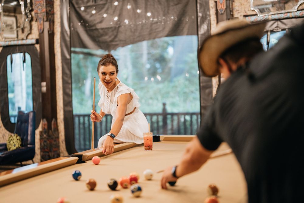 People playing billiards in upscale room with scenic tropical views through large windows.