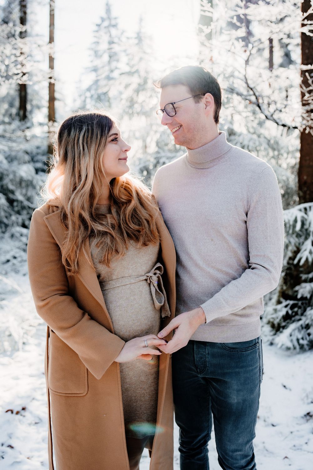 A couple shares intimate moments in a snowy winter forest setting wearing casual clothing.