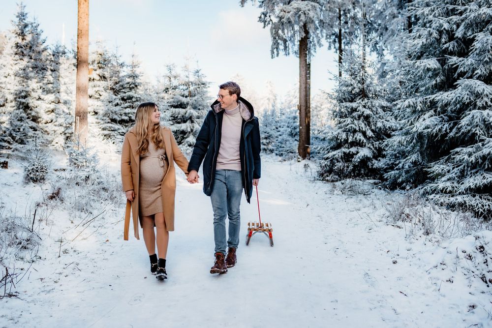 Two people walking hand in hand on a snowy winter path through evergreen trees on a bright cold day.