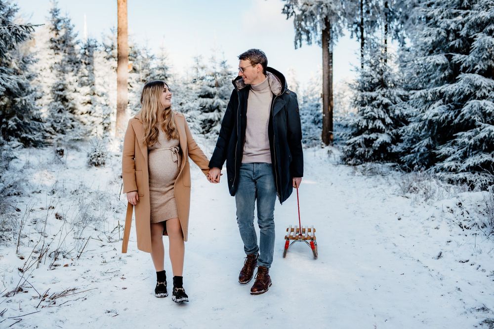 People walking through a snowy forest landscape while pulling a wooden sled behind them.