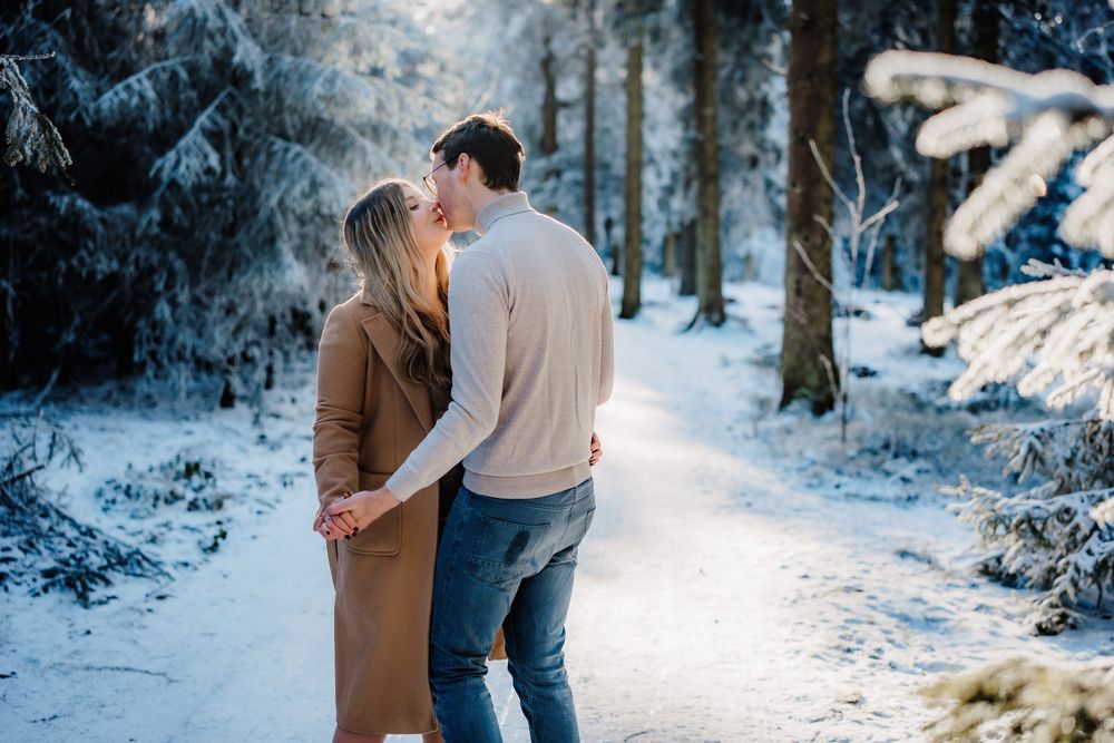 Couple walks together through a snowy wooded trail on a winter afternoon.