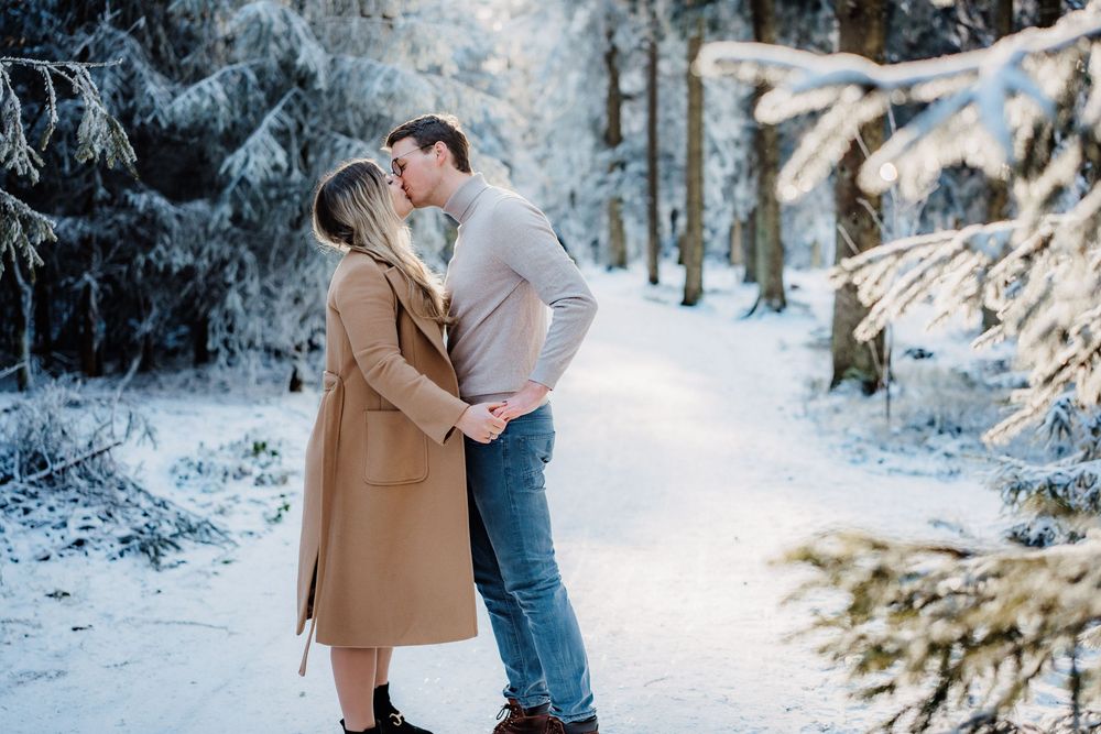 A couple embraces in a snowy forest setting surrounded by frost-covered evergreen trees.